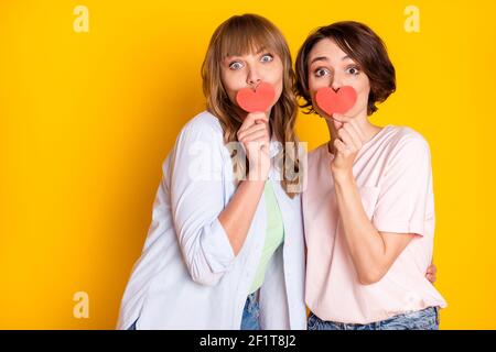 Ritratto di due adorabili ragazze mano tenere piccolo cuore cartolina che copre la bocca isolata su sfondo giallo Foto Stock