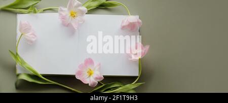 Apri il libro di schizzo con la cornice floreale di tulipani di rose. Mockup di album aperto con fogli bianchi vuoti su uno sfondo delicato di colore verde pallido. Vista dall'alto piatta lo Foto Stock