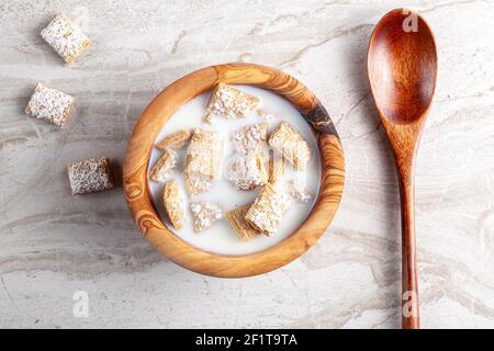 Un semplice concetto di colazione con una ciotola di cereali di grano di dimensione morso ghiacciato nel latte sul piano cucina in marmo. Un cucchiaio di legno è lì per mangiare. Foto Stock