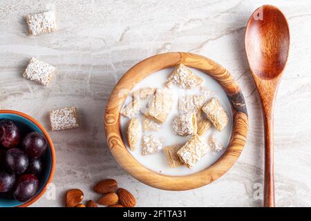 Un semplice concetto di colazione con una ciotola di cereali di grano di dimensione morso ghiacciato nel latte sul piano cucina in marmo. Ci sono uva e noci come antipasti Foto Stock