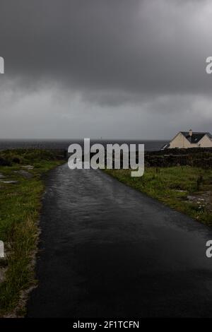 Paesaggio con cielo grigio scuro, nuvole di pioggia e strada grigia che conduce in oceano tempestoso Foto Stock