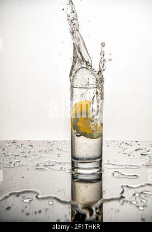 Limone splash isolato su sfondo bianco. Il limone cade e si spruzzi in un bicchiere d'acqua Foto Stock