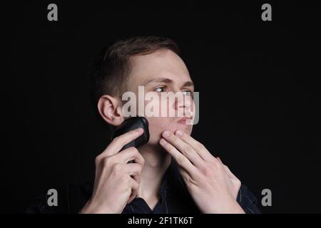 Un giovane europeo rasa il viso con un rasoio elettrico Foto stock - Alamy