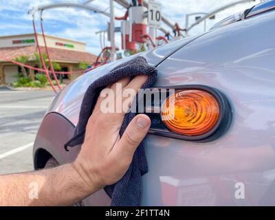 La mano dell'uomo pulisce l'auto con un panno in microfibra nero. Pulire a mano la superficie dell'auto Foto Stock