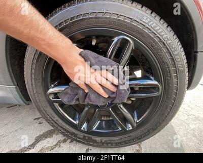 La mano dell'uomo pulisce l'auto con un panno in microfibra nero. Pulire a mano la superficie dell'auto Foto Stock