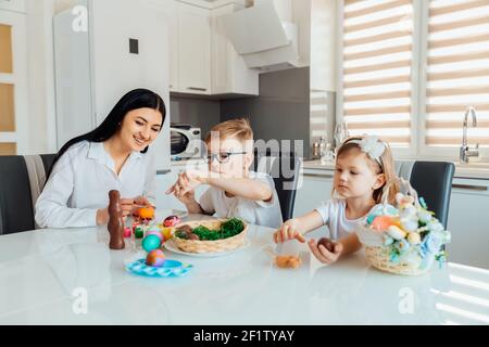 Madre con i capretti verniciano le uova di Pasqua. Felice famiglia che fa decorazioni per le vacanze di Pasqua Foto Stock