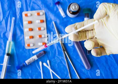 Un medico con un guanto di lattice che tiene il vaccino dentro un ago per siringa con provette per analisi del sangue sullo sfondo Foto Stock