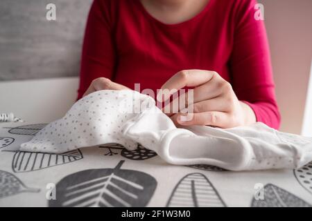 Primo piano sulle mani di donna caucasica sconosciuta che tiene e Impacchettamento vestiti del bambino a casa - donna incinta che prepara il jumpsuit per il bambino in camera luminosa - m Foto Stock