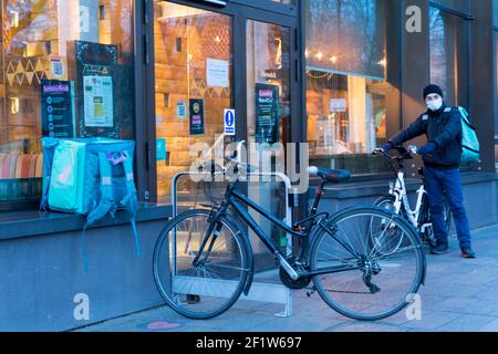 Deliveroo rider in attesa fuori dal ristorante per i loro alimenti di ordine del cliente Foto Stock