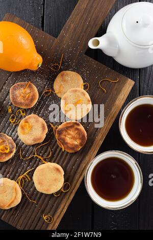 Biscotti fatti in casa con scorza di limone serviti con tè puerh su vista dall'alto su pannelli di quercia scuro a coste Foto Stock