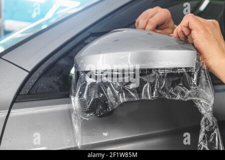 Montaggio PPF sullo specchietto retrovisore esterno. La pellicola di protezione della vernice è un rivestimento protettivo in poliuretano per la verniciatura dell'auto. Foto Stock