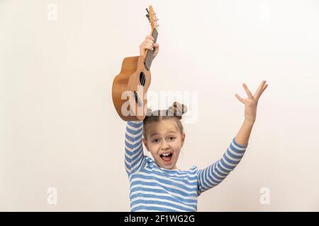 ragazza teen che tiene un ukulele di chitarra e ridendo su un sfondo chiaro Foto Stock