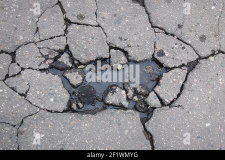 Grandi crepe su strada asfaltata piena d'acqua, danni alla superficie stradale in primavera Foto Stock