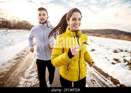 Primo piano di due amici sportivi attivi che corrono in una giornata invernale nella natura innevata. Foto Stock