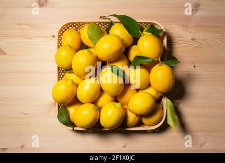 Un sacco di limoni in un cesto su uno sfondo di legno. Vista direttamente dall'alto Foto Stock