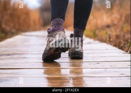 i piedi della ragazza camminano sul passerella di legno con gli stivali da trekking sopra giorno piovoso Foto Stock