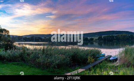 Un colorato tramonto sul paesaggio del lago con piccole barche a remi il primo piano Foto Stock