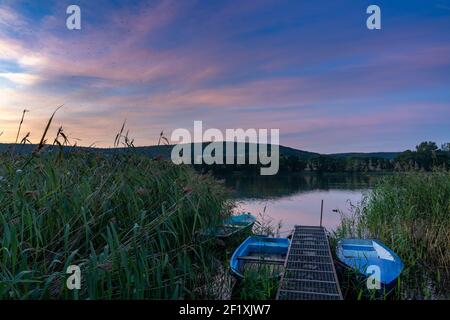 Un colorato tramonto sul paesaggio del lago con piccole barche a remi il primo piano Foto Stock