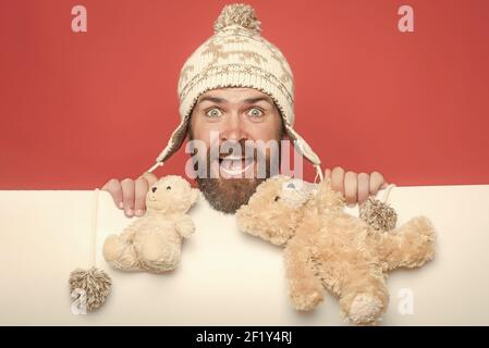 Divertente uomo e compleanno. Celebrazione e festa. Hipster con giocattolo su sfondo bianco rosso. Ragazzo con faccia felice in cappello invernale Foto Stock