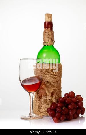 Vino rosso in bicchiere con uva e bottiglia su fondo bianco. Foto Stock