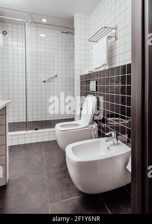 Bagno moderno interno combinato con servizi igienici. Il bagno e la doccia sono coperti da piastrelle bianche e nere pavimento nero Foto Stock