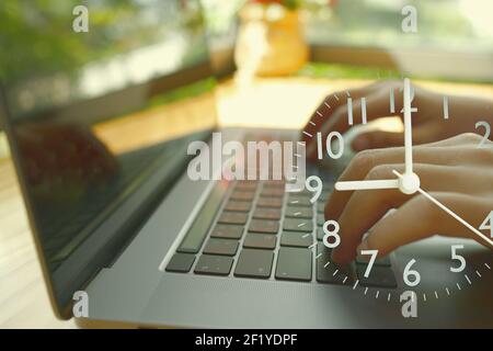 Una mano astratta che digita un laptop e un orologio analogico che mostra l'ora di inizio del luogo di lavoro. Foto Stock