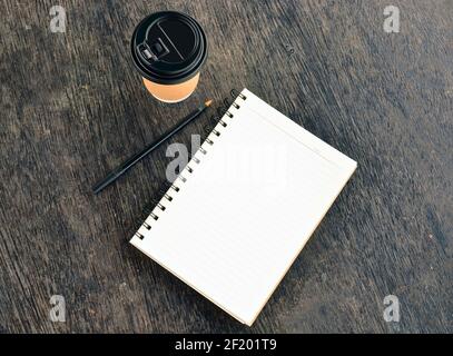 Blocco note con tazza da caffè usa e getta e penna su tavolo di legno Foto Stock