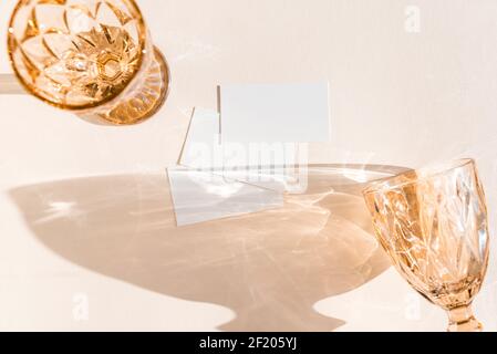 Scena di vita still con bicchieri da vino su sfondo beige in luce del sole e in bianco affari, biglietto d'auguri, invito mockup. Lunghe ombre dure. Foto Stock