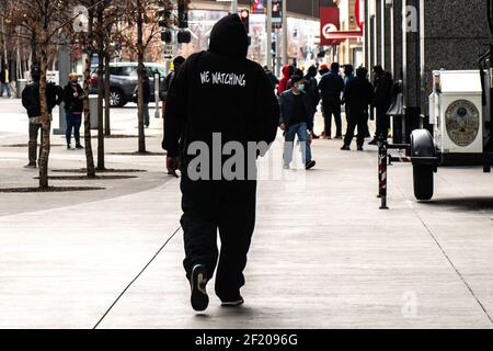 Minneapolis, Stati Uniti. 09 marzo 2021. Un uomo con una sweathert che dice, 'noi guardando,' cammina in centro il 9 marzo 2021 a Minneapolis, Minnesota. La selezione della giuria è prevista per iniziare oggi nel processo dell'ex ufficiale di polizia di Minneapolis Derek Chauvin nella morte di George Floyd lo scorso maggio. Foto: Chris Tuite/ImageSPACE Credit: Imagespace/Alamy Live News Foto Stock