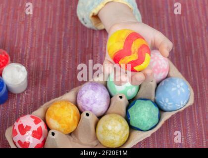 Piccola mano che tiene dipinto uovo di pasqua. Uovo di Pasqua in un bambino mani. Creatività artistica. Vista dall'alto Foto Stock