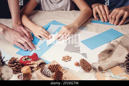 Le mani di una madre caucasica e di sua figlia stanno tagliando i fiocchi di neve di carta con le forbici. Fatti a mano, decorazioni natalizie, attività invernale familiare. Clos Foto Stock