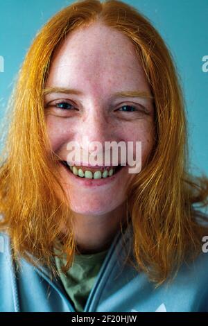 Tilburg, Paesi Bassi. Studio-ritratto di una donna sorridente e dai capelli rossi che indossa una camicia di marca su sfondo grigio. Foto Stock