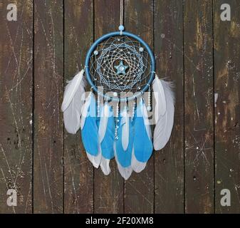 Bellissimo boho dreamcatcher fatto a mano con piume bianche e blu. Sfondo mistico con catcher sogno contro tavole di legno, esoterico, etnico e s. Foto Stock