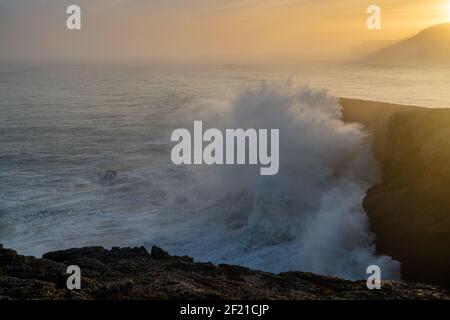 Una vista di enorme tempesta che si infrangono le onde oceaniche riva e scogliere all'alba Foto Stock