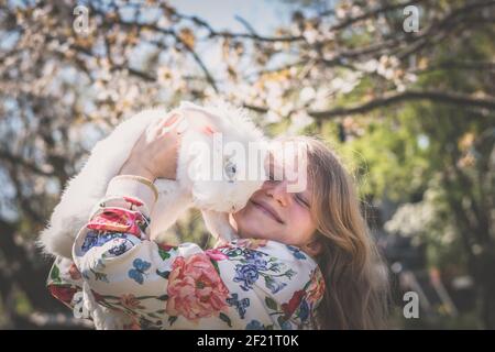 Adorabile bella ragazza con lunghi capelli biondi abbracciando bianco Pasqua animale di coniglio Foto Stock