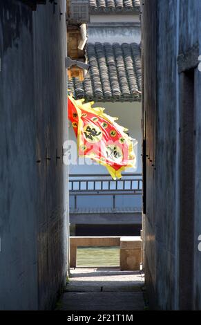 Bandiera rossa e gialla soffia nel vento, rompendo i grigi degli edifici e vicoli in questa città vecchia cinese. Yuehe in Jiaxing. Foto Stock