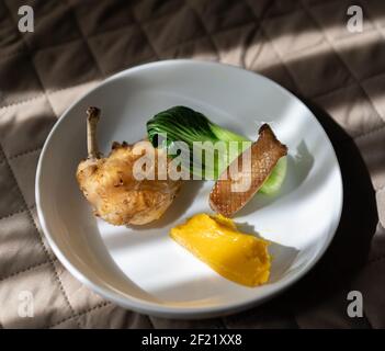 Un pollo arrosto con un bok choy, un'ostrica arrosto e una purea di zucca su un piatto bianco Foto Stock