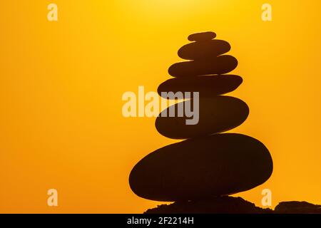 Profilo a piramide di ciottoli bilanciato sulla spiaggia. Astratto caldo tramonto bokeh con Mare sullo sfondo. Pietre Zen sulla spiaggia di mare, meditazione, spa Foto Stock