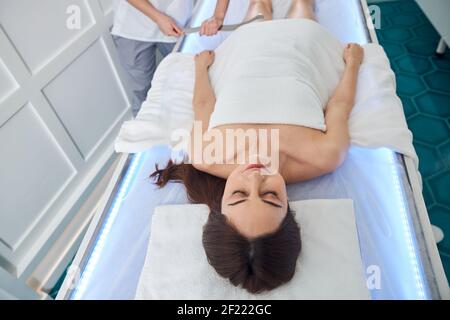 Massagista che raschia la gamba femminile con uno strumento lungo di gua sha Foto Stock