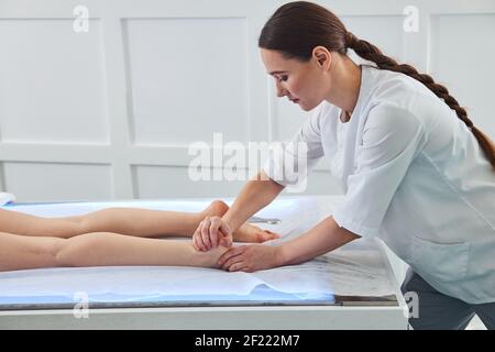 Il massaggiatore femminile sta eseguendo una compressione del tallone Foto Stock