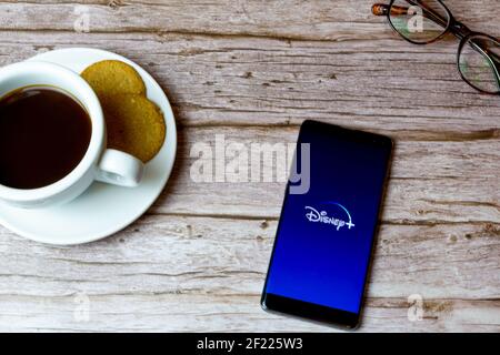 Un telefono cellulare o un telefono cellulare posato su un legno tavolo con l'app disney plus che apre anche un caffè e bicchieri Foto Stock