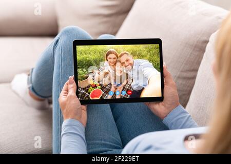 Giovane donna che ha una conversazione remota con la famiglia felice al picnic, usando il computer del tablet a casa Foto Stock