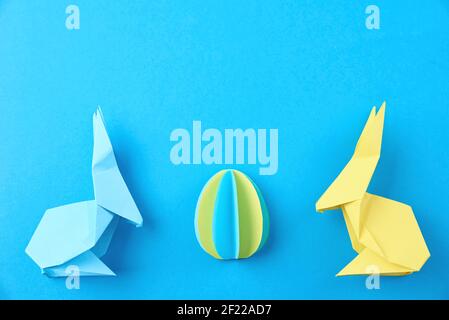 Due conigli di carta origami Esater e uovo colorato su sfondo blu. Festa di Pasqua Foto Stock
