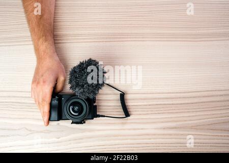 Un uomo che tiene la mano sulla piccola macchina fotografica nera professionale con un microfono su un tavolo di legno Foto Stock