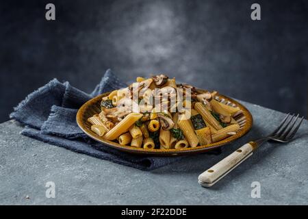 Penne di pasta con funghi arrostiti, aglio e zucchine. Cucina italiana su tavolo di marmo blu. Foto Stock