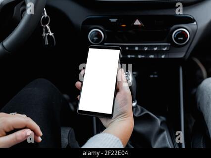 Giovane conducente che utilizza smartphon in auto durante la guida o il parcheggio. Mockup di un telefono cellulare con schermo bianco isolato nel han Foto Stock