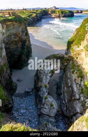 Calda serata d'oro su una spiaggia di sabbia con jagged e. scogliere frastagliate Foto Stock