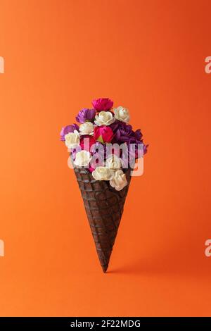 Cono gelato nero con fiori colorati su sfondo luminoso. Composizione estiva minima. Foto Stock