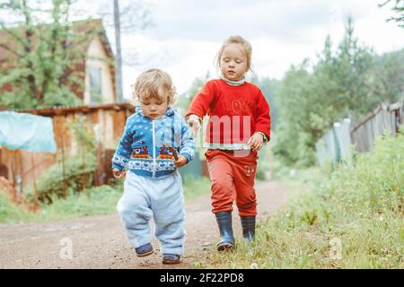 sorella e fratello camminano per la strada in un piccolo villaggio tra le case Foto Stock