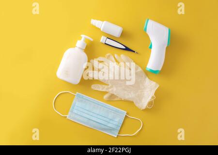 Guanti medici, disinfettante, termometro, disinfettante per le mani e maschera chirurgica su sfondo giallo Foto Stock